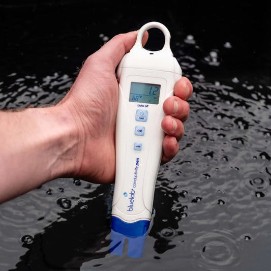 Bluelab Conductivity Pen held in one hand while taking a reading from a reservoir